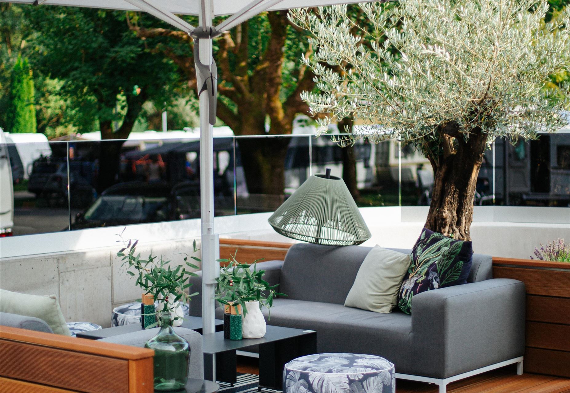 Ein gemütlicher Außenbereich mit einem grauen Sofa, einem großen Sonnenschirm und gepflegten Pflanzen. Der Raum ist modern eingerichtet und lädt zum Entspannen ein.