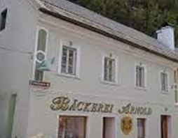 Eine Bäckerei mit dem Namen "Bäckerei Arnold" in einem charmanten Gebäude. Im Hintergrund ist ein grüner Hang sichtbar.