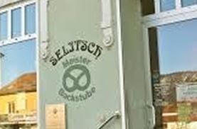 Eine Bäckerei mit einem hellen Eingang und einem großen Schild. Die Fenster sind einladend und zeigen die Vielfalt der angebotenen Backwaren.