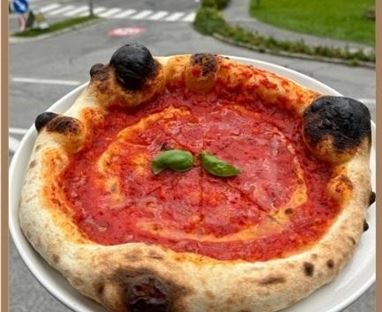 Eine frisch gebackene Pizza mit roter Soße und frischem Basilikum. Der Rand ist knusprig und hat kleine angebrannte Stellen.