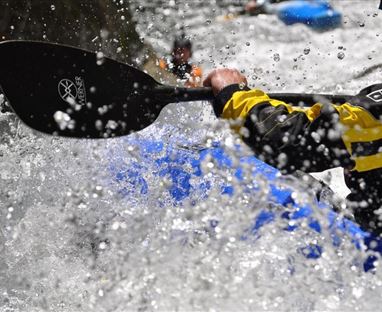 Ein Paddler im Wasser mit einem kräftigen Spritzwasser. Im Hintergrund sind einige Kajaks zu sehen.