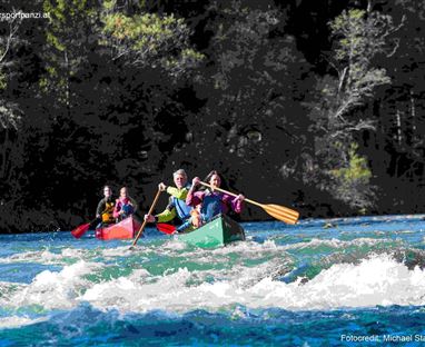 Eine Gruppe von Menschen paddelt in kanus auf einem Fluss. Wellen und üppige Bäume umgeben die Szene.