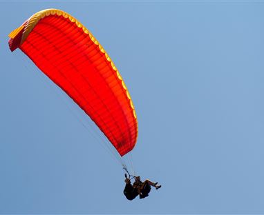 Zwei Personen gleiten mit einem roten Gleitschirm durch den blauen Himmel. Es ist ein schöner, klarer Tag.