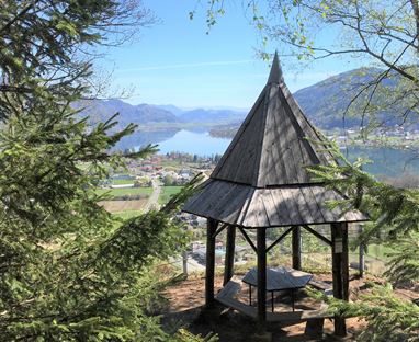 Ein Aussichtspunkt mit einem Holzpavillon umgeben von Bäumen. Im Hintergrund ist ein schöner Blick auf einen See und die umliegenden Berge.