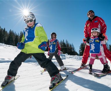 Eine fröhliche Skigruppe mit Kindern auf der Piste. Sie tragen bunte Ski-Ausrüstung und genießen einen sonnigen Tag im Schnee.