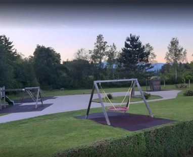 Un parco giochi moderno con altalene e uno scivolo, circondato da prati verdi e alberi. L'ambiente tranquillo invita a giocare e rilassarsi.