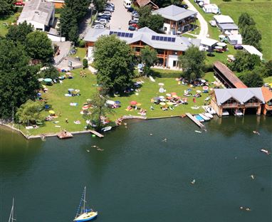 Eine grüne Wiese am Wasser mit Liegestühlen und Booten. Umgeben von Gebäuden und Bäumen, bietet der Ort eine entspannte Atmosphäre.