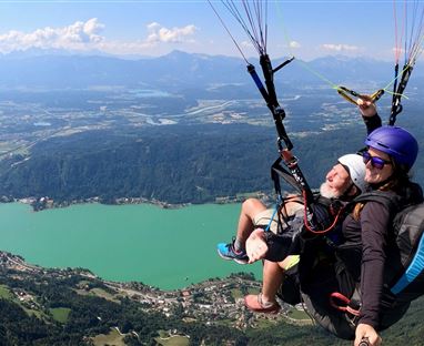 Ein Tandemflug beim Paragliding über einem malerischen See und Bergen. Die Aussicht ist atemberaubend und der Himmel ist klar.