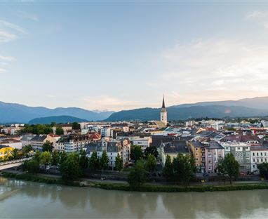 Eine malerische Stadt am Fluss mit einer Kirche im Mittelpunkt. Im Hintergrund sind sanfte Berge und ein klarer Himmel sichtbar.