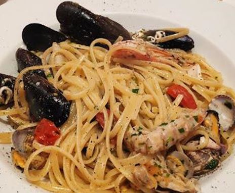A plate of spaghetti topped with mussels, shrimp, and tomatoes. The dish is served on a white plate and looks appetizing.