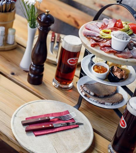 A cozy table with two beer glasses and a festive stand full of meat platters and side dishes. The tablecloth is made of wood and looks inviting.
