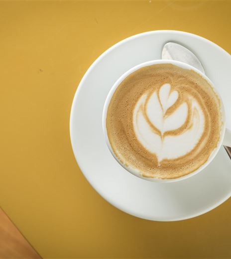 Una tazza di cappuccino con un motivo artistico di latte su un piattino bianco. Lo sfondo è giallo e crea un vivace contrasto.