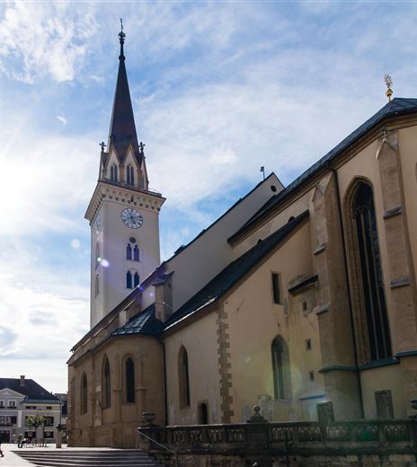 Eine historische Kirche mit einem hohen Turm in einer Stadt. Das Licht der Sonne strahlt durch den Himmel und beleuchtet die Gebäude in der Umgebung.