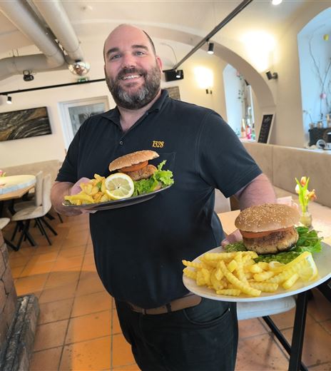 Un cameriere gentile porta due piatti con hamburger e patatine. Sullo sfondo si vede un ristorante accogliente.