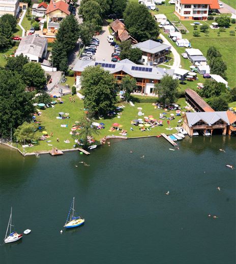 A green meadow by the water with lounge chairs and boats. Surrounded by buildings and trees, the place offers a relaxed atmosphere.