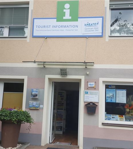 Un edificio con un'insegna per l'informazione turistica. Davanti alla porta c'è un vaso di fiori e sono visibili materiali informativi.