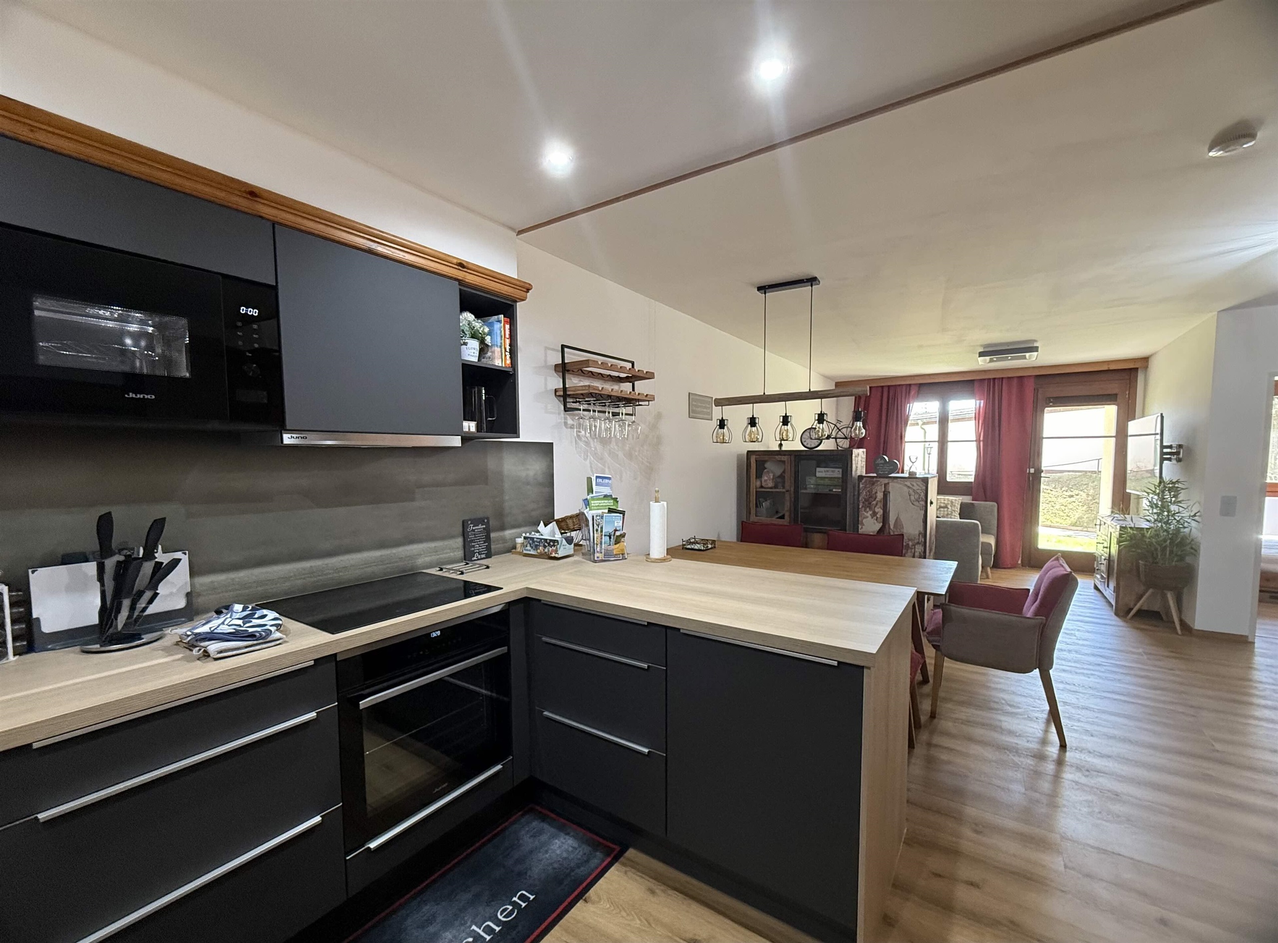 Eine moderne Küche mit einer Holzarbeitsfläche und schwarzen Schränken. Der Raum ist hell und freundlich mit einem offenen Wohnbereich.
