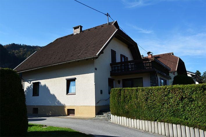 Ein zweigeschossiges Haus mit braunem Dach und Balkon. Umgeben von gut gepflegten Hecken und einem ruhigen Weg.