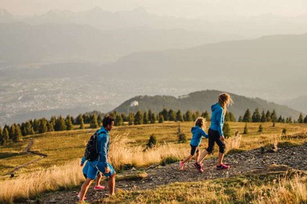 Eine Gruppe Kinder wandert auf einem Bergpfad. Im Hintergrund ist eine atemberaubende Landschaft mit schneebedeckten Bergen und einem klaren Himmel zu sehen.