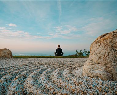 A peaceful landscape with gravel and a few large stones. In the background, a person is sitting and enjoying the view.