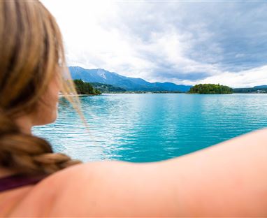 A beautiful lake with clear, blue water and gentle hills in the background. A person is looking at the landscape and enjoying the view.