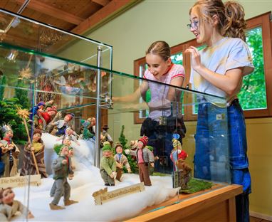 Zwei Mädchen betrachten eine Vitrine mit detailreichen Figuren. Die Figuren sind Szenen aus dem Alltagsleben nachempfunden.