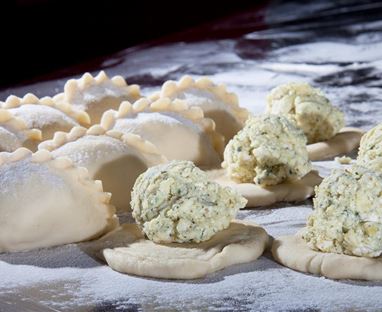 Ein Tisch mit frischen Teigtaschen und Füllungen auf einer bemehlten Fläche. Die Teigtaschen sind gleichmäßig geformt und bereit zum Kochen.