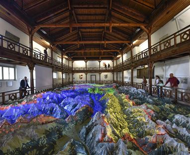 Ein großer, farbiger 3D-Relief der Berge ist im Raum zu sehen. Besucher betrachten das Modell von verschiedenen Ebenen aus.