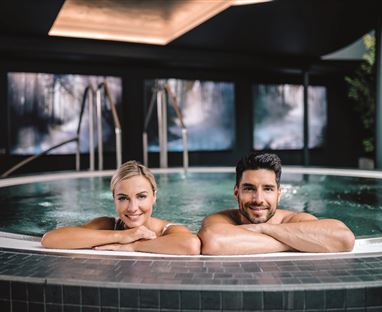 A couple relaxes in a modern hot tub. Elegant pictures and a cozy atmosphere are visible in the background.