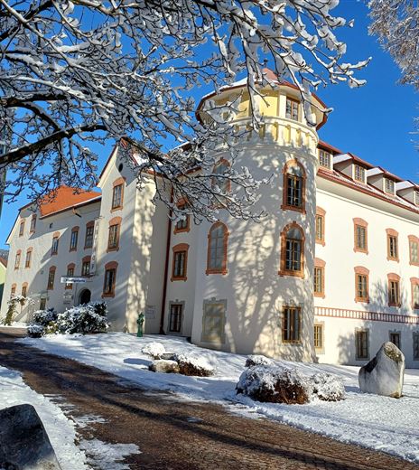 Ein schönes, historisches Gebäude im Schnee. Die Umgebung ist winterlich mit schneebedeckten Bäumen und einem blauen Himmel.