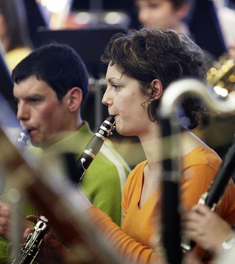 A group of musicians is playing in an orchestra. In the foreground, two people with clarinets can be seen as they focus on the performance.