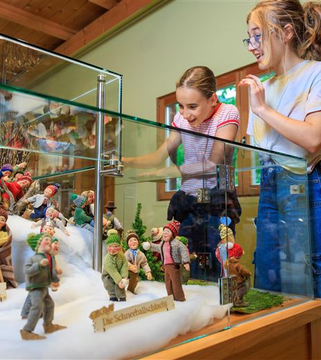Due ragazze osservano una vetrina con figure dettagliate. Le figure riproducono scene della vita quotidiana.