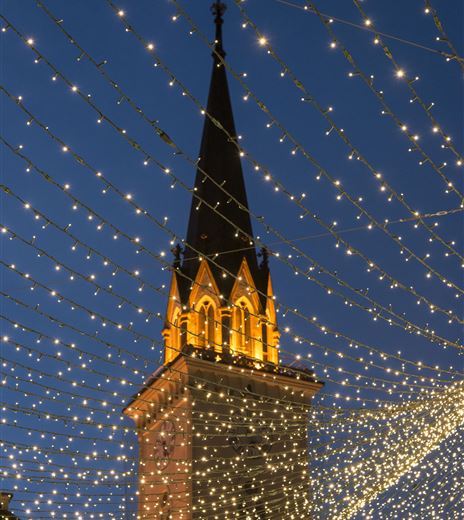 Ein schön beleuchteter Kirchturm vor einem nächtlichen Himmel. Lichterketten ziehen sich kunstvoll über den Platz.