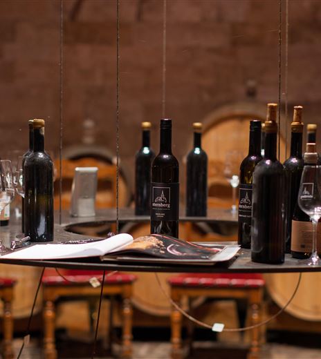 Eine elegante Weinstube mit einer Vielzahl von Weinflaschen und Gläsern auf einem Tisch. Im Hintergrund sind Weinfässer und rustikale Stühle zu sehen.