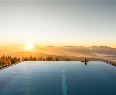 Ein moderner Pool mit Blick auf die Berge bei Sonnenaufgang. Die goldenen Sonnenstrahlen spiegeln sich im Wasser.