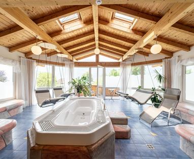 Ein gemütlicher Wellnessbereich mit einem Whirlpool und modernen Liegen. Große Fenster lassen viel Tageslicht herein und schaffen eine entspannte Atmosphäre.