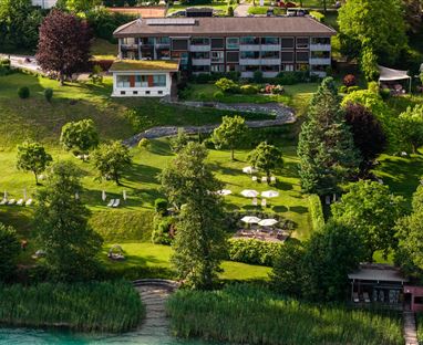 Un paesaggio giardino verde con alberi e sdraio. Sullo sfondo si trova un edificio moderno.