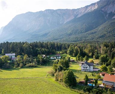 A picturesque landscape with houses and green meadows, surrounded by majestic mountains. The sky is clear and nature is lush and inviting.