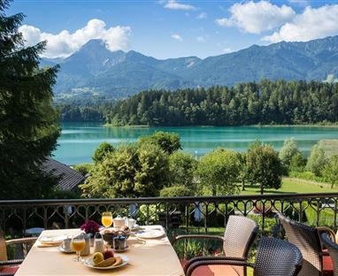 Eine schöne Aussicht auf einen See mit Bergen im Hintergrund. Auf dem Tisch sind Frühstücksgerichte und Getränke gedeckt.