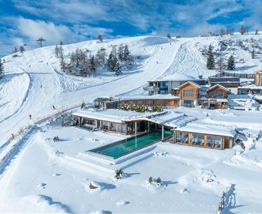 Un moderno chalet immerso in un paesaggio coperto di neve. In primo piano è visibile una piscina, circondata da montagne innevate.