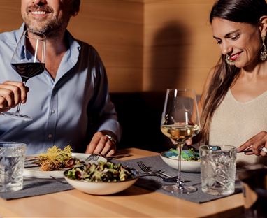 A beautiful dinner couple enjoys an elegant meal in a modern restaurant. They hold wine glasses in their hands and have a selection of delicious dishes on the table.