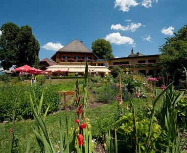 Un bel giardino davanti a un edificio con ombrelloni e un paesaggio verde. Il cielo è blu con alcune nuvole.