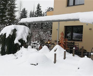 Un giardino innevato davanti a una casa. La neve copre gli alberi e il terreno.