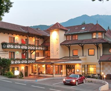 Ein charmantes Hotel mit einem traditionellen Design und einem einladenden Eingang. Im Hintergrund sind majestätische Berge zu sehen.