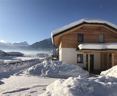 Una moderna casa di legno nella neve con montagne sullo sfondo. Il paesaggio è tranquillo e invernale.