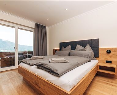 Ein modernes Schlafzimmer mit einem großen Doppelbett und eleganter Holzverkleidung. Große Fenster bieten einen Blick auf die Berge.
