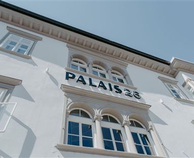 Ein elegantes Gebäude mit der Aufschrift "PALAIS 26". Es ist weiß gestrichen und hat große Fenster.