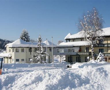 Ein malerisches Gebäude im Schnee, umgeben von schneebedeckten Bäumen. Der klare Himmel verleiht der Szene eine ruhige Winteratmosphäre.
