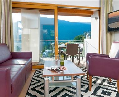 A stylish living room with a purple sofa and an armchair. Large windows offer a beautiful view of the landscape.