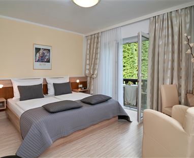 A cozy room with two beds, bright walls, and modern furniture. The space has access to a balcony that is surrounded by curtains.